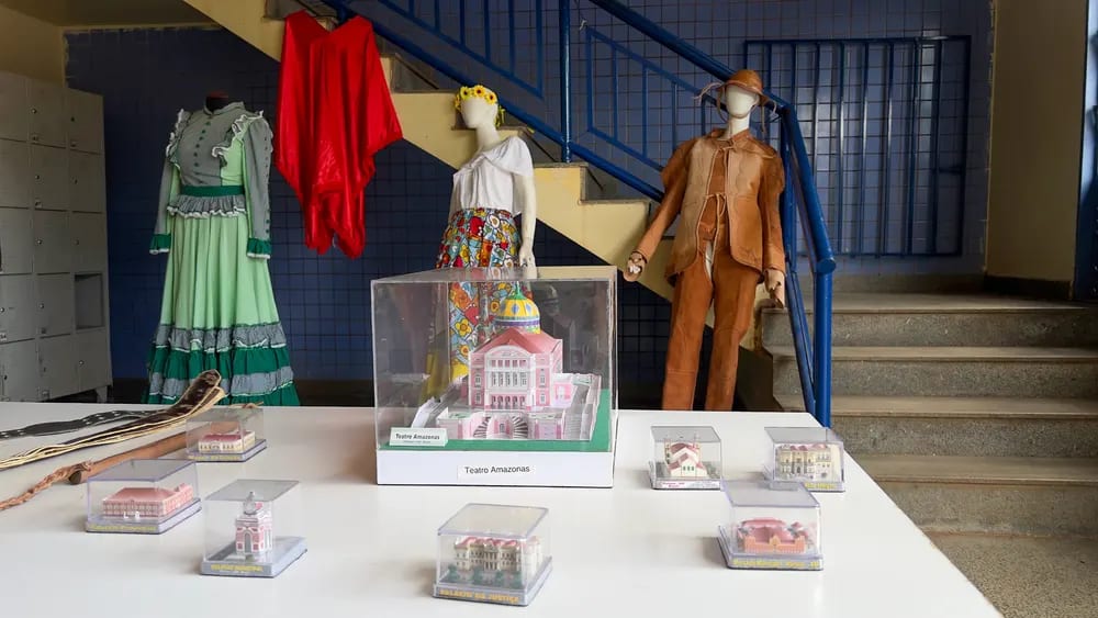 Mostra de trajes típicos em manequins ao lado de maquetes protegidas por redomas de acrílico