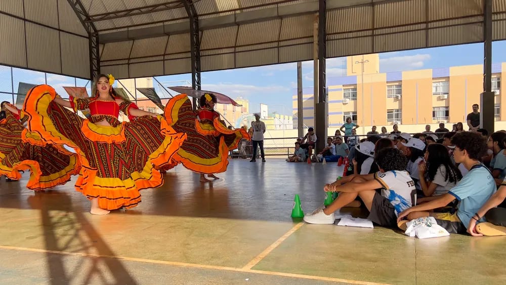Roda de dançarinas com saias coloridas girando na quadra da escola