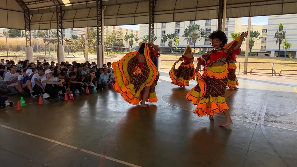 Dançarinas em trajes típicos executam a coreografia na quadra da escola
