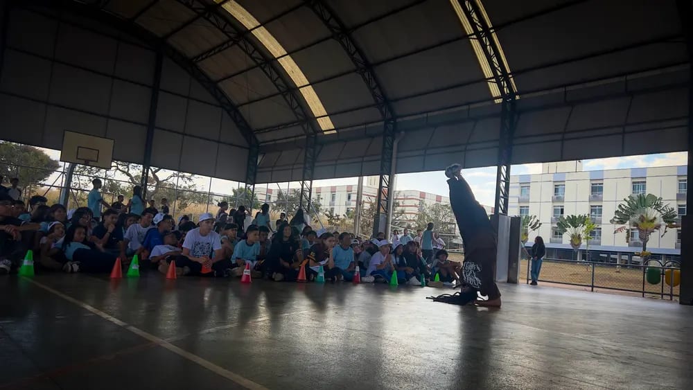 Público sentado acompanha a apresentação na quadra da escola