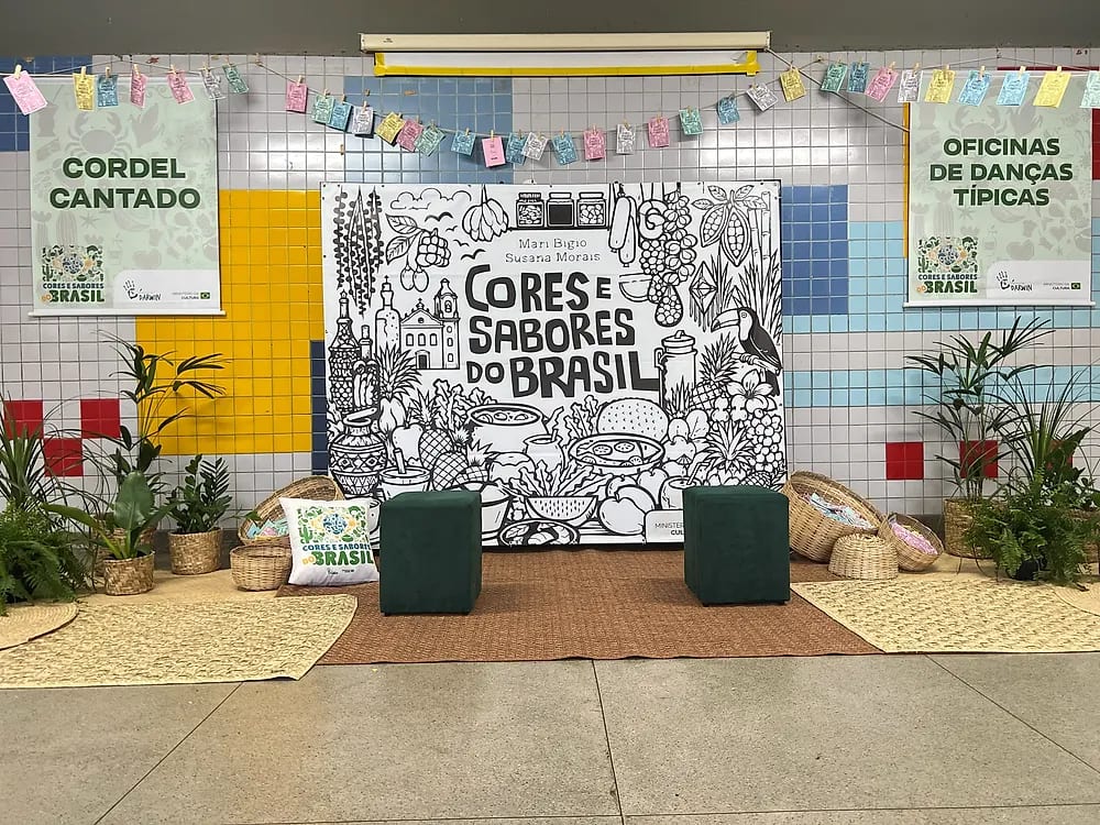 Cenário do projeto montado no pátio da escola: painel ilustrado do Cores e Sabores do Brasil, varal de cordéis, plantas, cestarias e faixas de Cordel Cantado e Oficinas de Danças Típicas